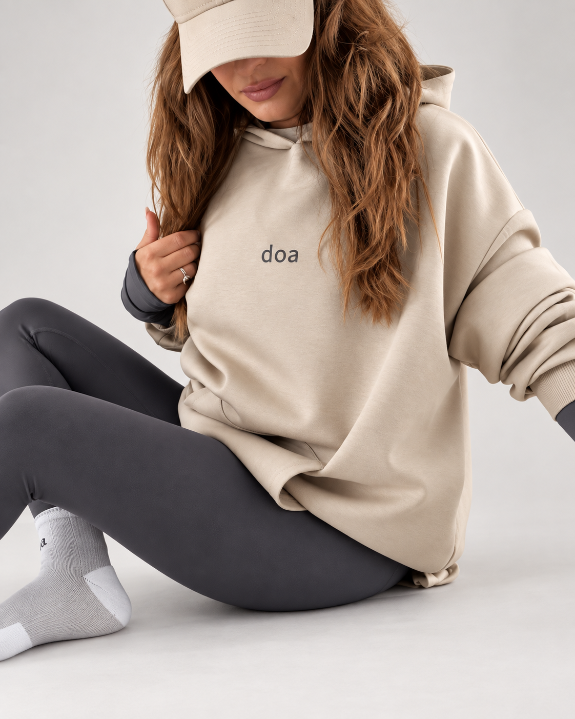 Woman wearing doa oversized hoodie in beige with grey leggings, seated.