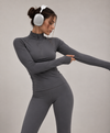 Woman wearing doa grey half-zip workout top with thumbholes and grey leggings, studio