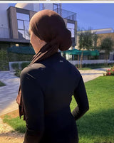 Woman in hijab wearing doa black half-zip workout top outdoors, back view