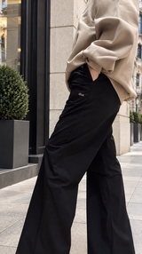 Close-up of doablack relaxed wide-leg trousers showing the fluid drape, styled with a beige jumper