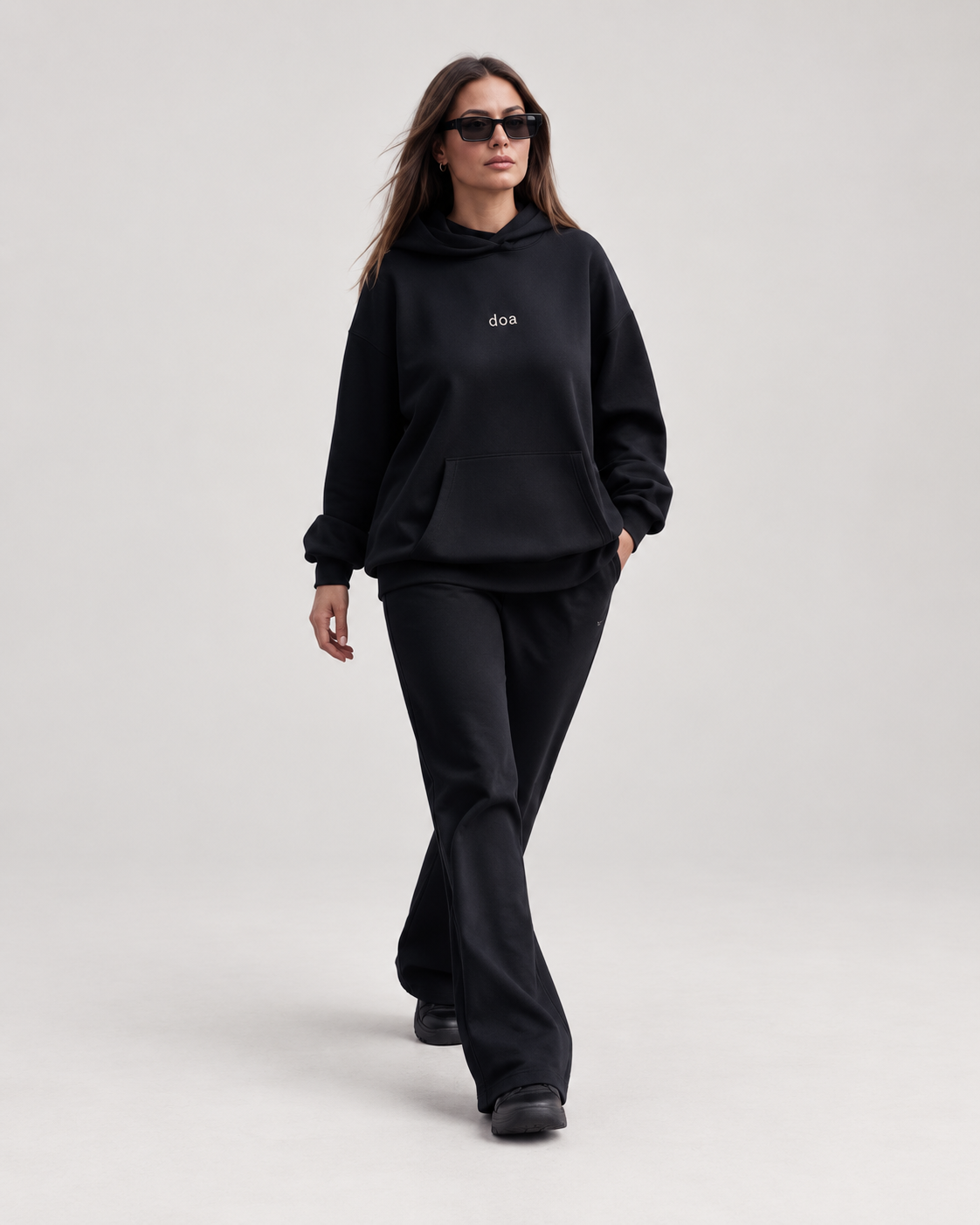 Woman wearing doa oversized hoodie in black with black relaxed trousers, front view