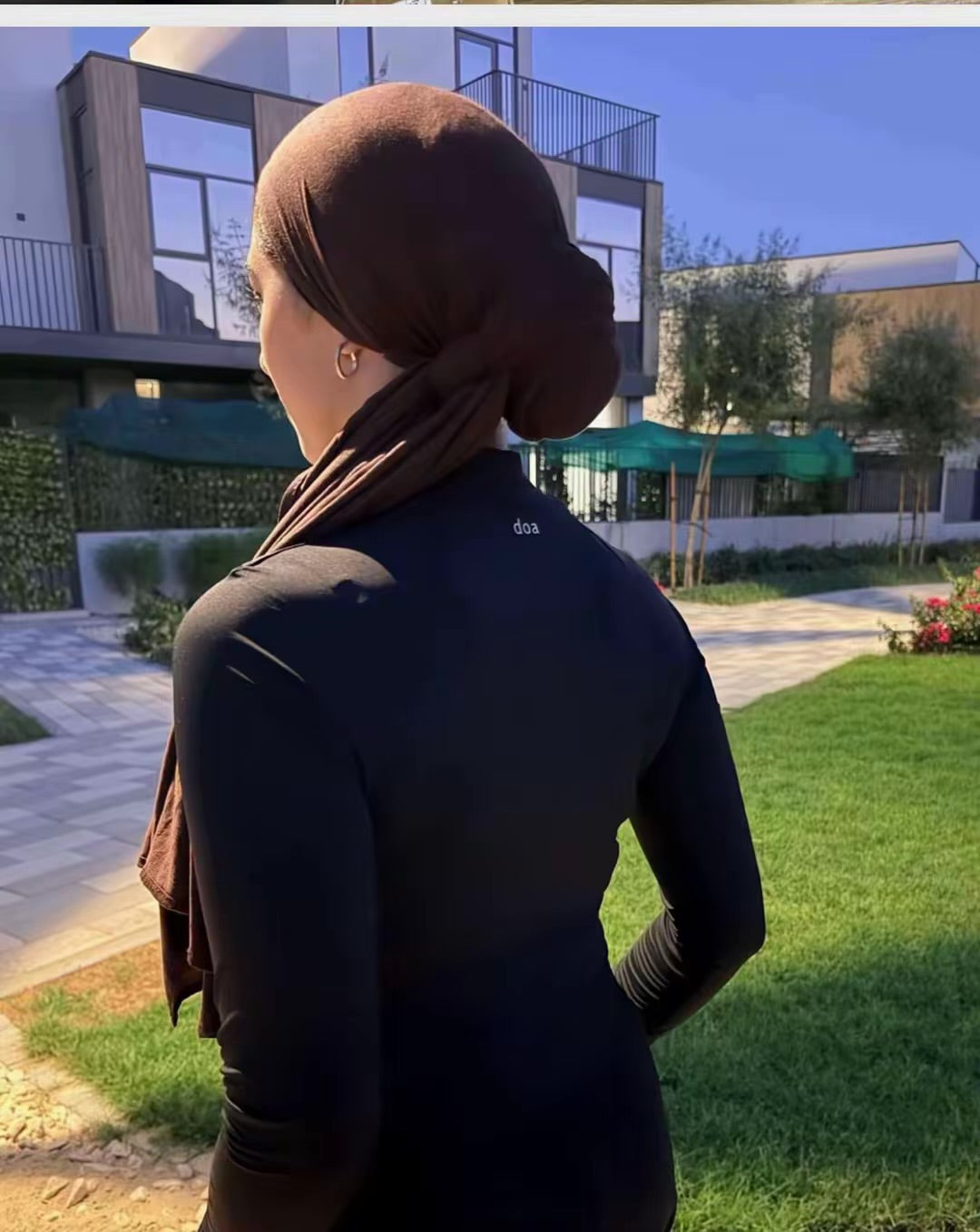 Woman in hijab wearing doa black half-zip workout top outdoors, back view