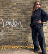 Woman wearing doa black relaxed wide-leg trousers against a brick wall in London
